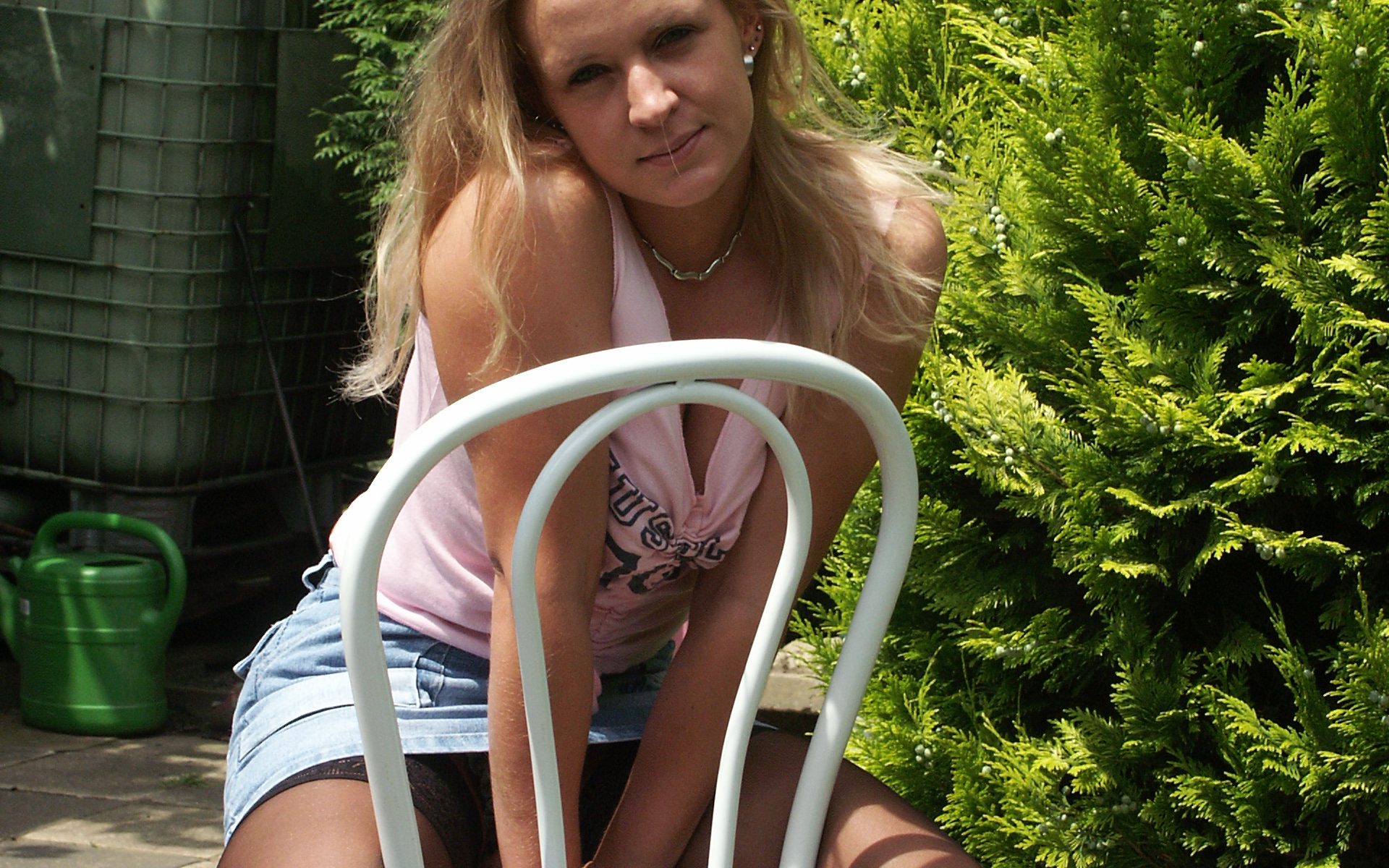 süße Blondine sitzt in Strapse und Minirock auf Stuhl im Garten